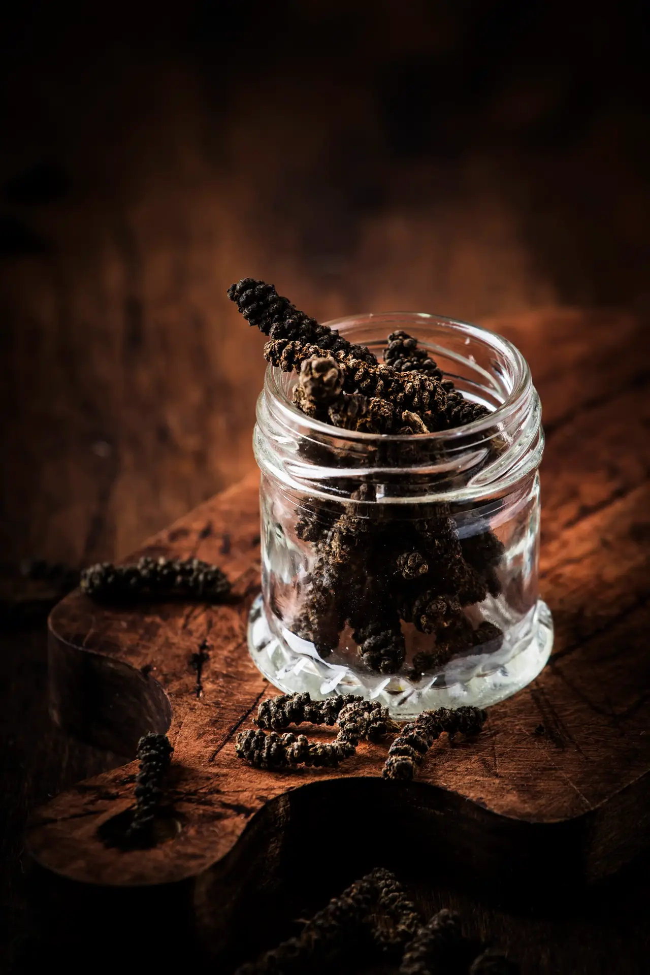Fragrant long pepper spilling out of glass jar, vintage kitchen table background, selective focus
